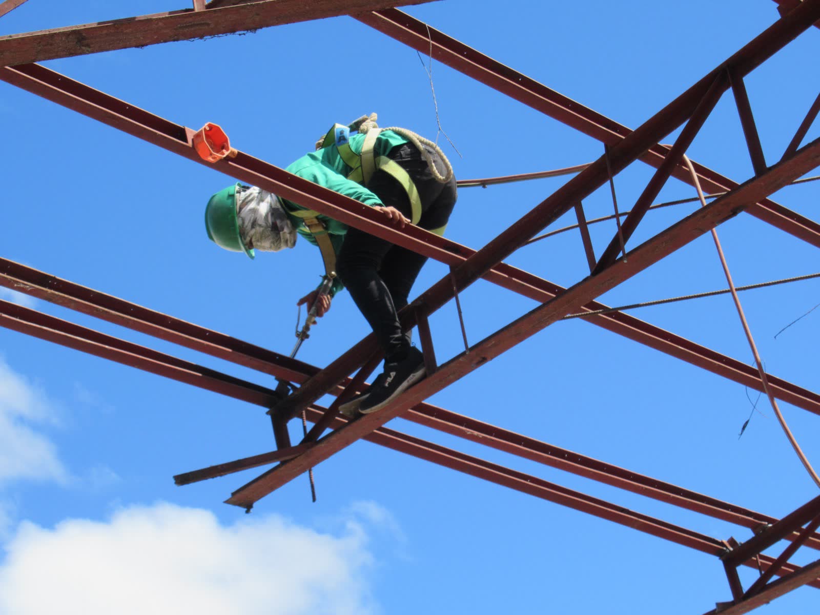 Welder in a green hard hat and PPE on a metal structure